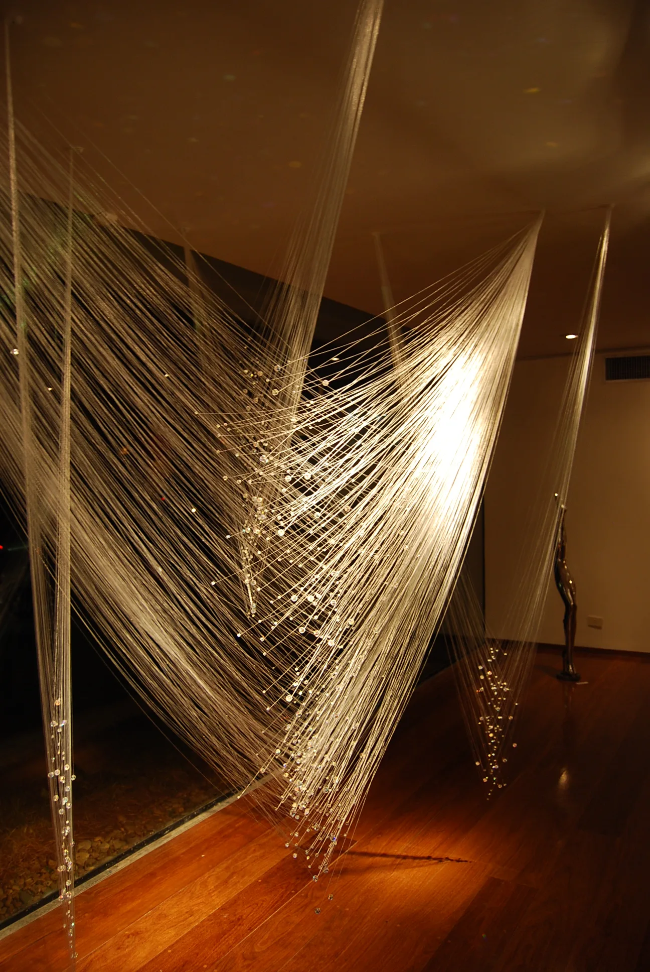 Fine threads strung with crystals catch warm light in a dark interior.